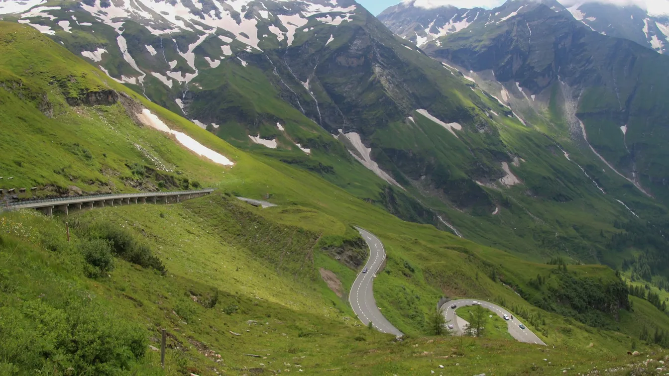 a winding road in the alps with mountains in the background