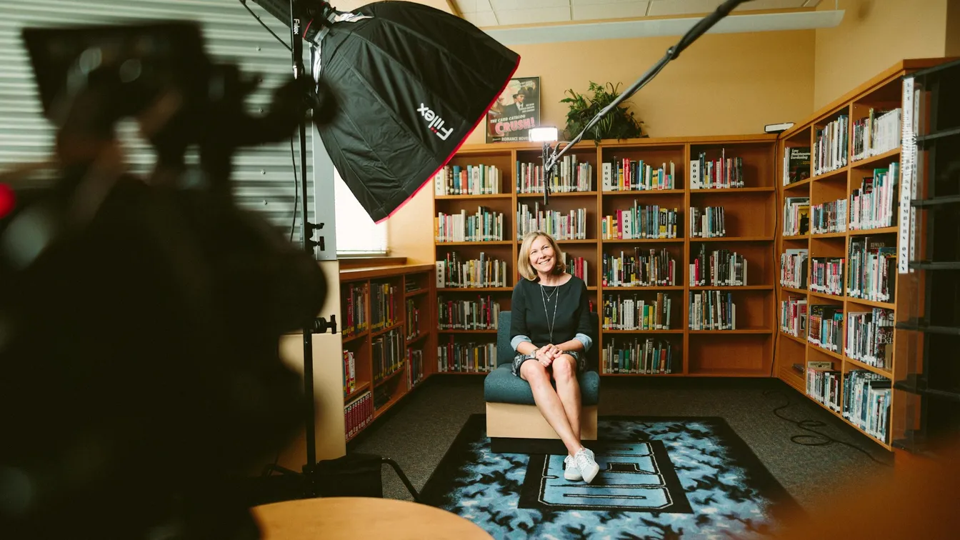 a woman sitting on a chair in a library with a camera